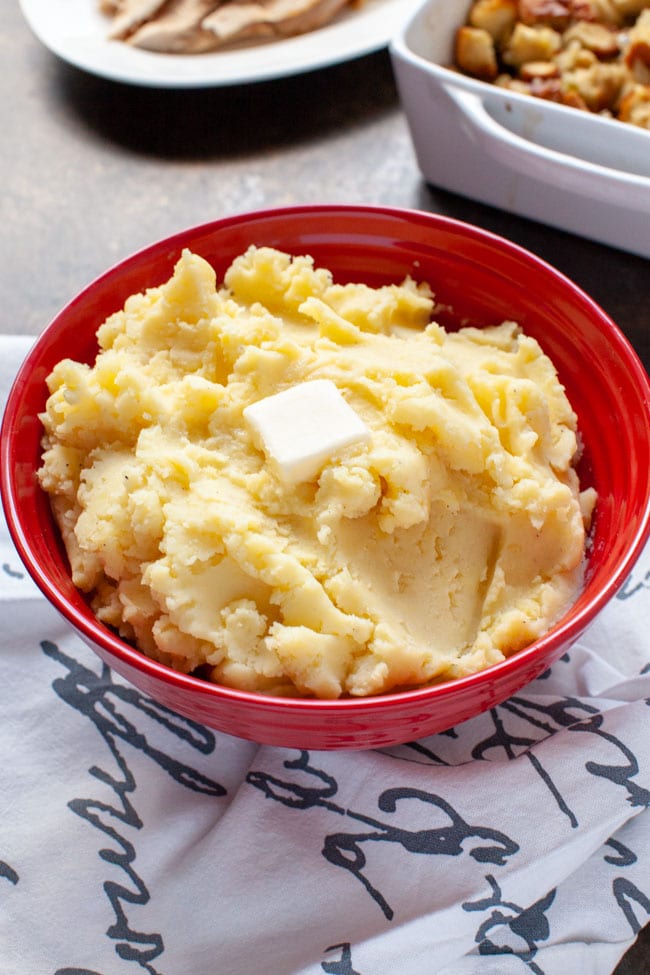 Perfect Mashed Potatoes from thelittlekitchen.net Mashed potatoes in a large red bowl with melted butter on top and other side dishes in the background