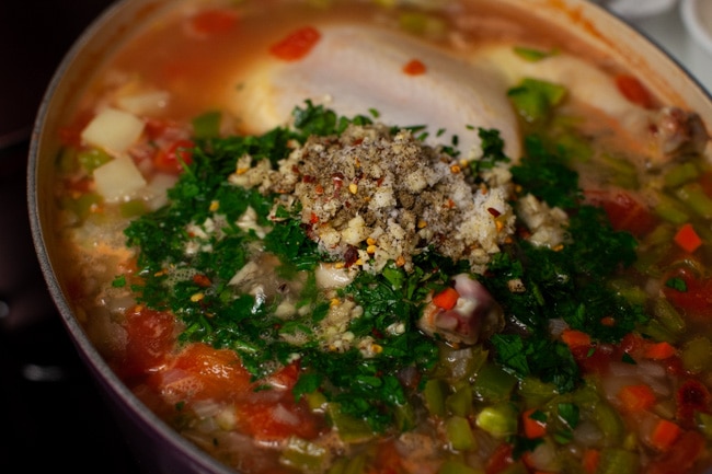 Spicy Chicken Soup from thelittlekitchen.net whole chicken in a soup pot with chopped parsley and other herbs on top