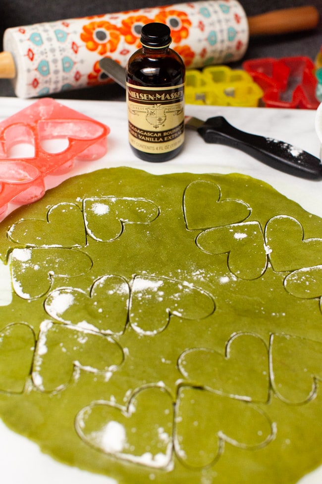 Matcha Cookies from thelittlekitchen.net Matcha Cookie dough with heart-shaped cookie cutter impressions with bottle of vanilla, spatula, cookie cutter, and rolling pins in background from thelittlekitchen.net