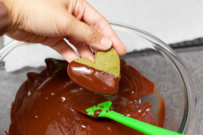 Matcha Cookies from thelittlekitchen.net Hand dipping heart-shaped Matcha Cookies into glass bowl of melted chocolate from thelittlekitchen.net