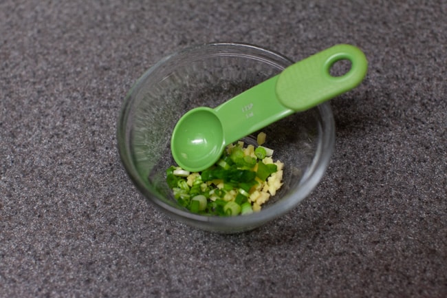 Vegetarian Dumplings from thelittlekitchen.net Minced ginger and green onions in a small glass bowl on a gray countertop with a green spoon