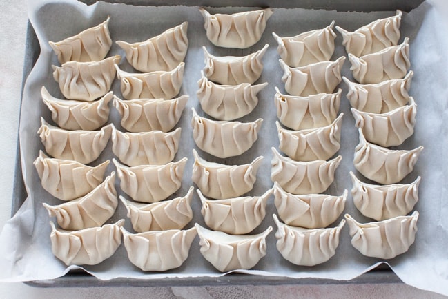 Vegetarian Dumplings from thelittlekitchen.net Parchment-lined baking sheet with uncooked Vegetarian Dumplings lined up from thelittlekitchen.net
