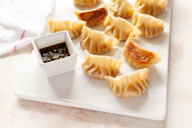 Vegan Dumplings from thelittlekitchen.net Vegan Dumplings on white serving tray with square dipping sauce bowl and kitchen towel in background from thelittlekitchen.net