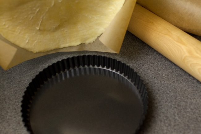 Black tart pan with parchment paper and rolling pin in background Black tart pan with parchment paper and rolling pin in background