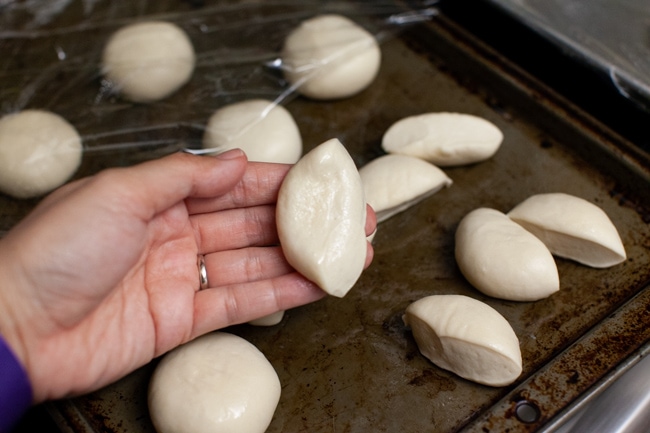Stuffed Bagel Bites from thelittlekitchen.net one Rhodes dinner rolls cut in half on a hand with other rolls on a baking sheet in the background