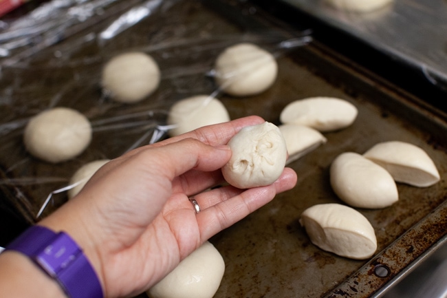 Stuffed Bagel Bites from thelittlekitchen.net a stuffed bagel bite on a hand with other rolls on a baking sheet in the background