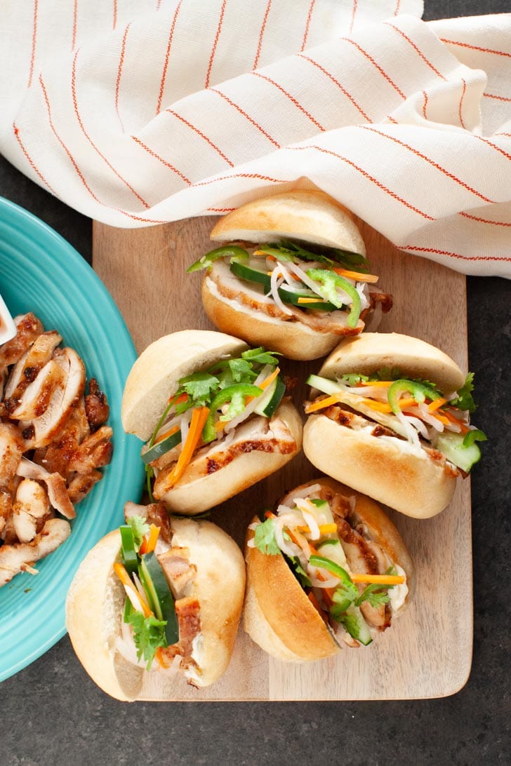 Lemongrass Chicken Banh Mi Sliders from thelittlekitchen.net chicken banh mi sliders on a wooden board with a plate of chicken on the left side