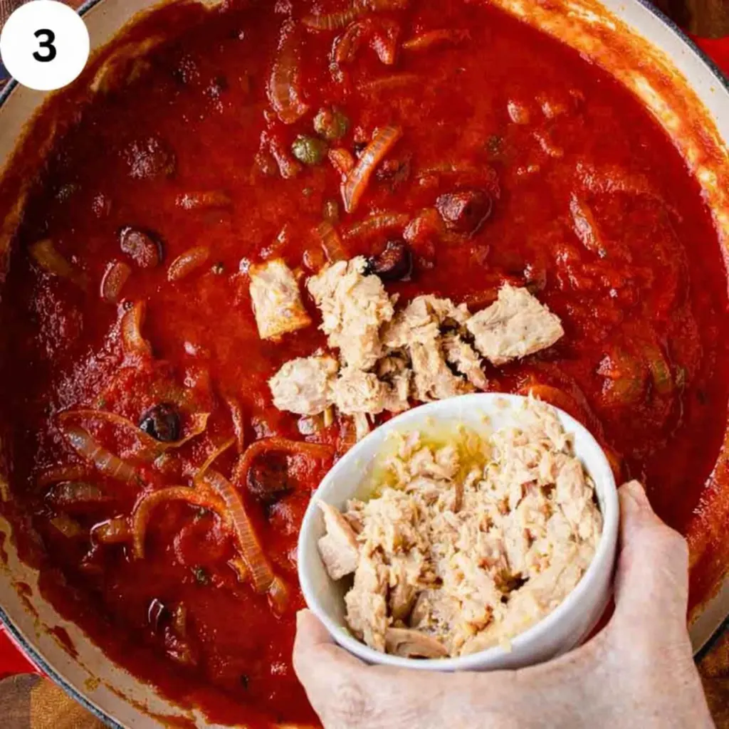 Folding tuna chunks into red sauce